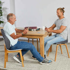 Two men chatting at a table, one using the TheraMed Total Spinal Support Backrest